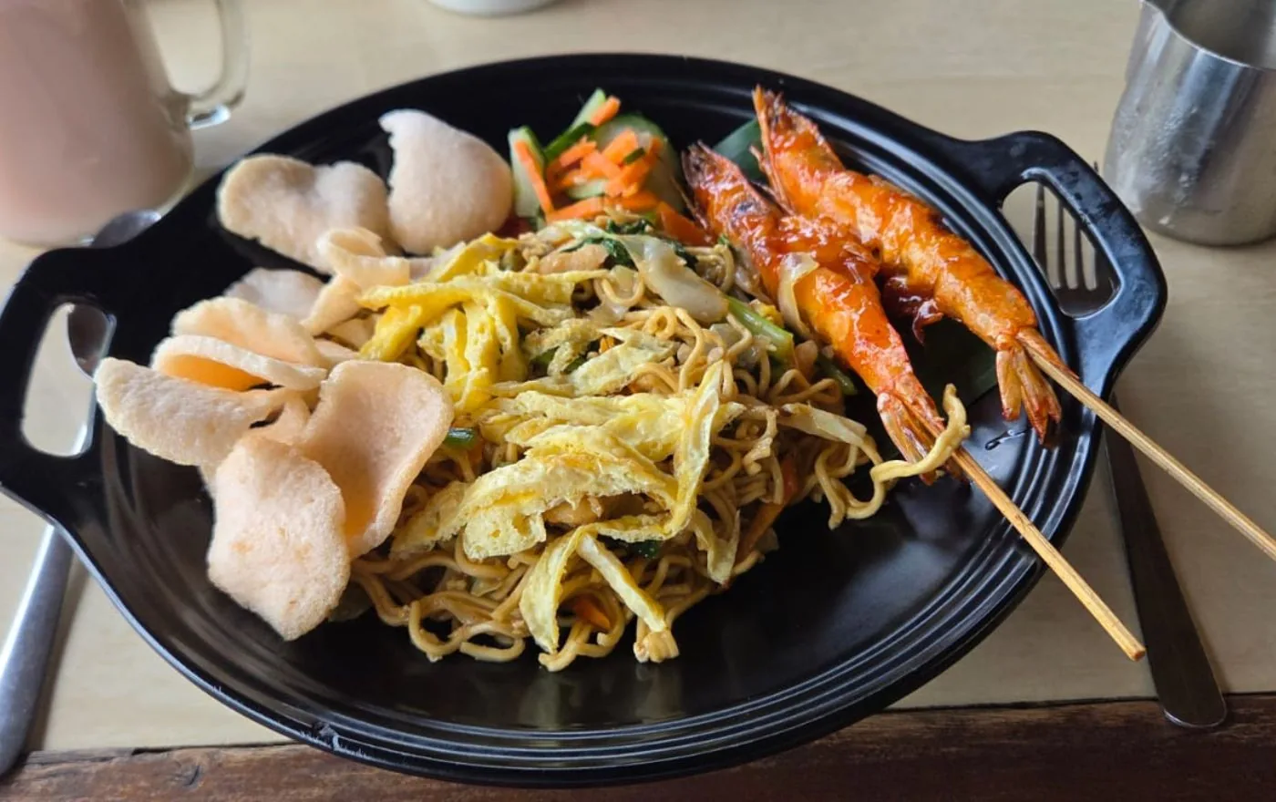 Mie Goreng fried noodles with a grilled shrimp skewer and vegetables on a plate