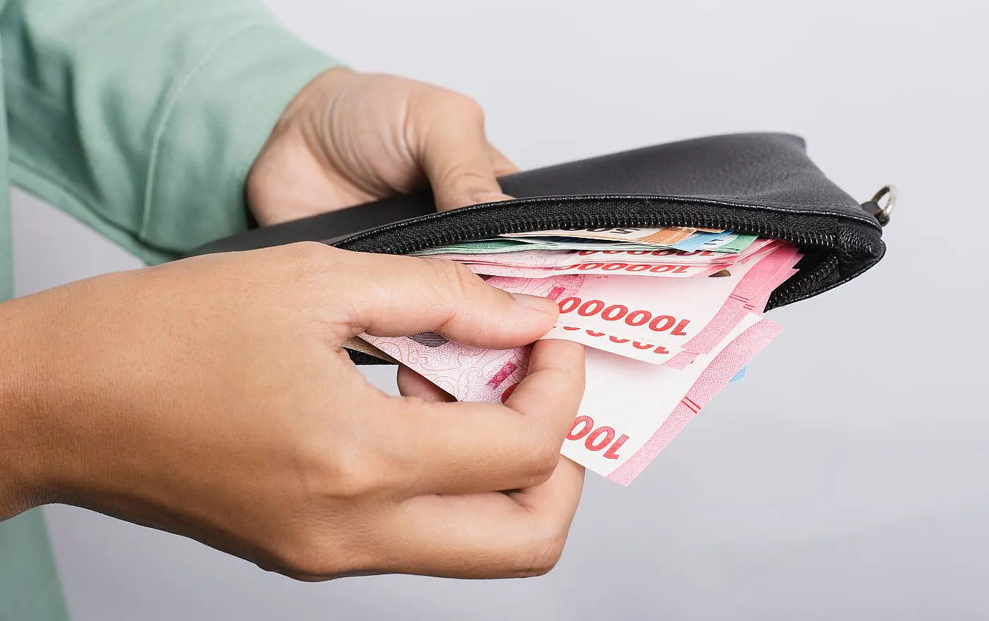 Person placing Indonesian Rupiah notes into a wallet while traveling in Bali